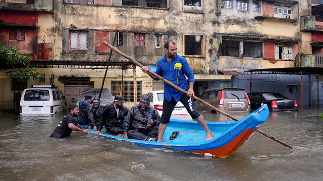 People move in a boat past partially submerged vehicles in Chennai 