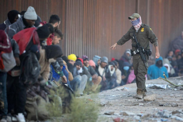 A U.S. Border Patrol agent asks immigrants to sit in a queue of those awaiting transport from the U.S.-Mexico border on Dec, 6, 2023, in Lukeville, Arizona. 