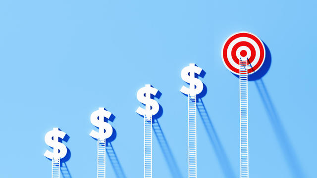 White Ladders Leaning Onto Dollar Signs And Bull's Eye Target on Blue Wall 