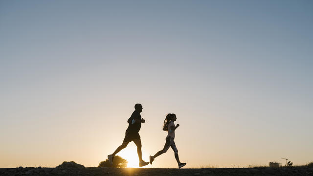 Silhouette of athlete and woman running against clear sky during sunset 