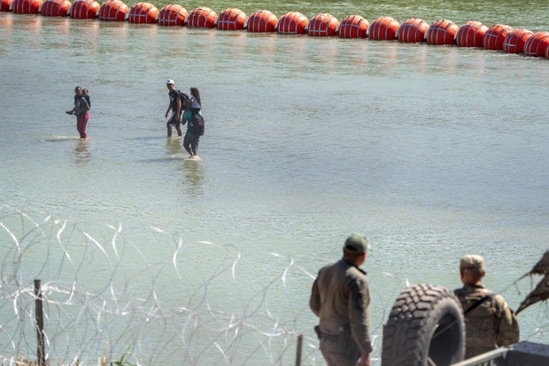 Texas Department of Public Safety highway patrol troopers look over the Rio Grande as migrants walk by a string of buoys placed on the water in Eagle Pass, Texas, on July 15, 2023.