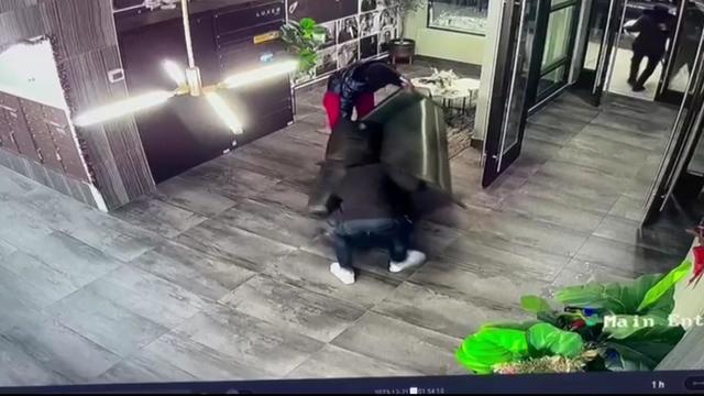 Surveillance footage shows two individuals carrying a couch out of an apartment building lobby. 
