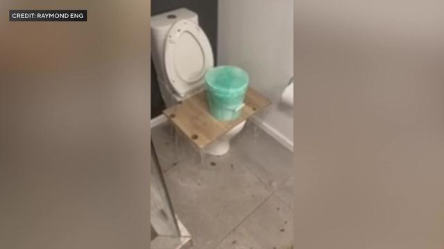 Cell phone video shows a toilet overflowing with water despite a piece of wood and a bucket being placed over the seat. 