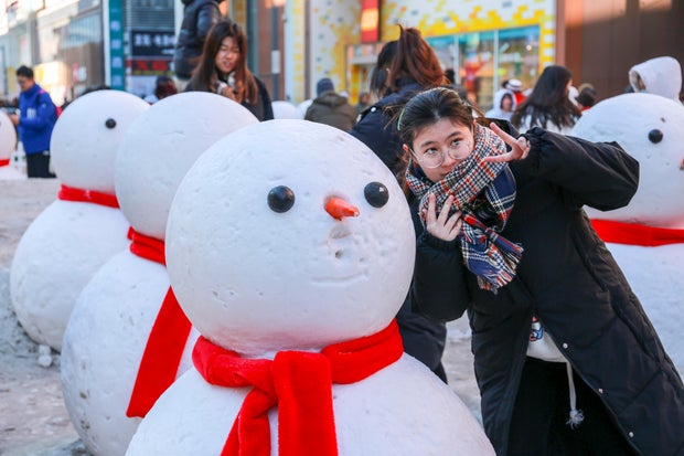 People pose for photos next to decorative snowmen at a shopping street on Dec. 25, 2023 in Shenyang, Liaoning Province, China