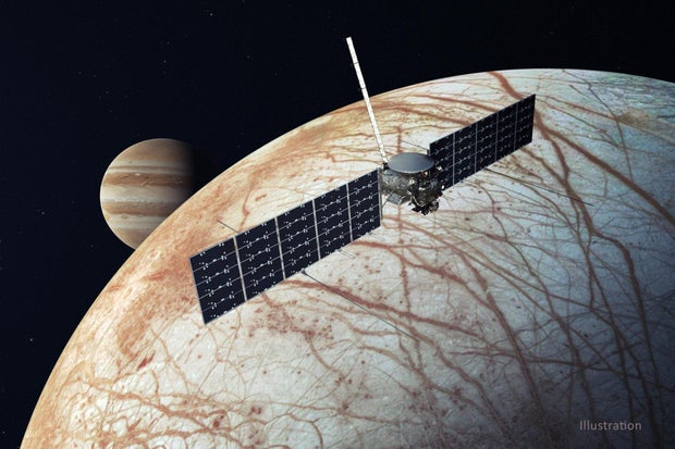 Illustration showing the Europa Clipper, a spacecraft with two solar panels, flying by Europa with Jupiter in the background