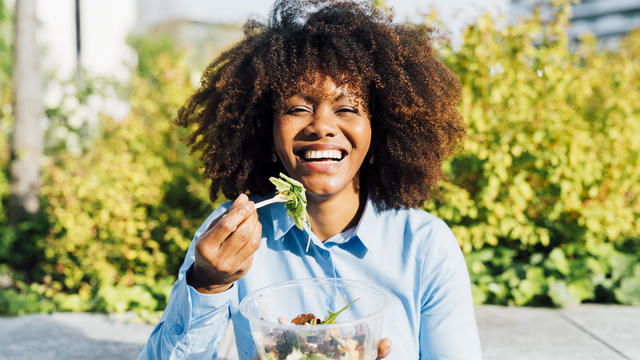 Happy businesswoman eating salad on sunny day 