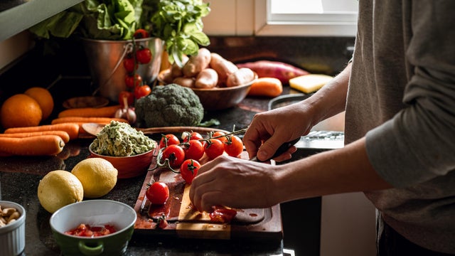 Human hands slicing tomatoes over a wooden table for a vegan meal 