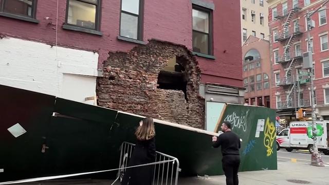 The exterior of a building in Little Italy. A facade has partially collapsed, revealing a hole in the exterior wall. 