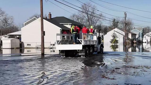 A high-water vehicle with rescue crews moves through a flooded Little Falls street. 