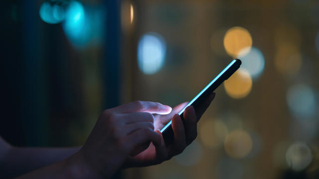 Close up of woman's hand using smartphone in the dark, against illuminated city light bokeh 