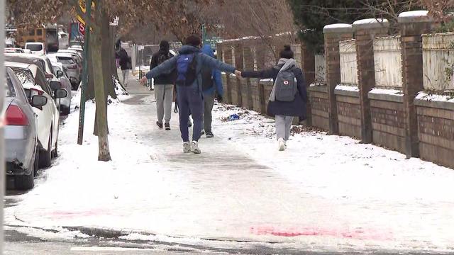 Pedestrians walk along an icy sidewalk. 