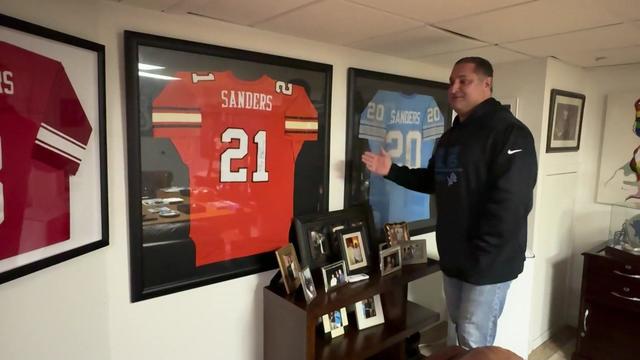 Rich Yevoli stands in his man cave and gestures at framed Sanders jerseys. 