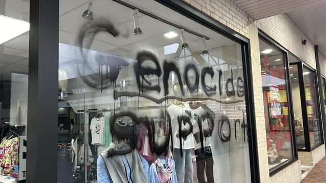The front window of a clothing shop with the words "genocide supporter" in black spray paint. 
