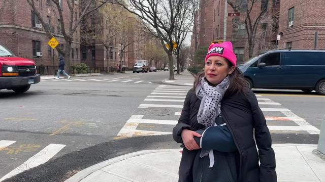Assemblymember Jessica González-Rojas, who has her arm in a sling due to a broken wrist, stands on a sidewalk corner. 
