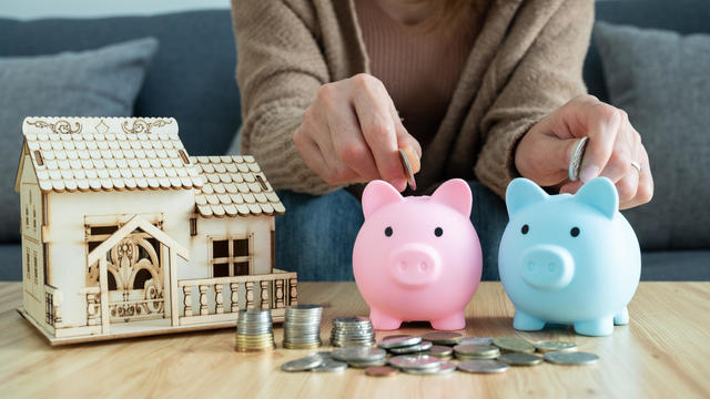 Cropped shot of woman while putting a coins into piggy bank for saving money. She planning to buy a new house. 