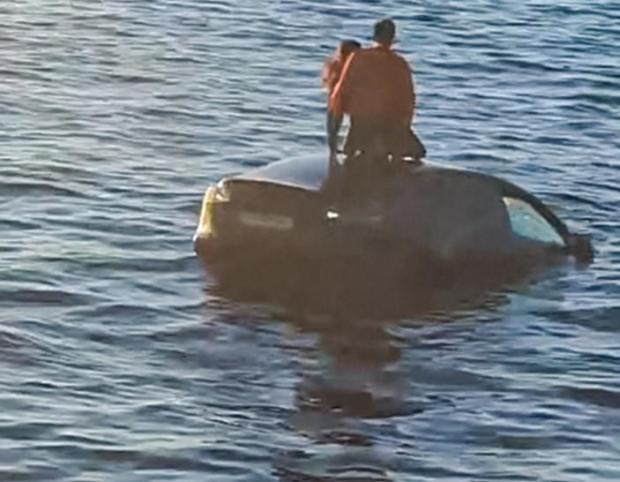Two people stand on top of a car in the water after driving into the Oslofjord on Feb. 1, 2024, in Oslo. 