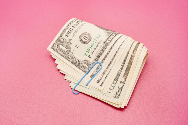 Directly above shot of a bundle of American Dollar bank notes with blue paper clip on pink background 