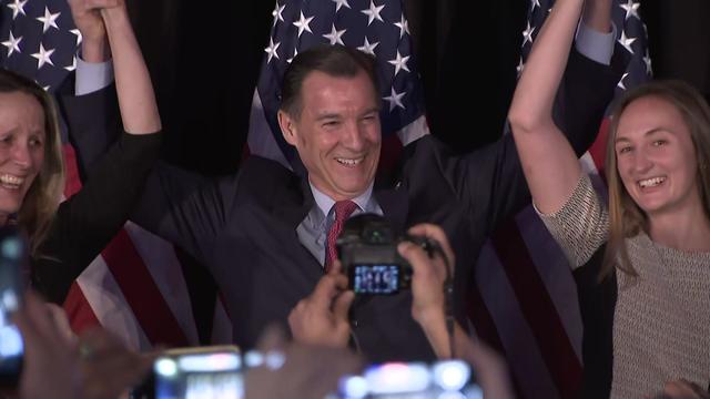 Tom Suozzi holds his family member's hands and raises his arms in victory after speaking to supporters. 