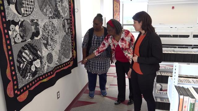 Nubian Heritage Quilters Guild co-founders Carolyn Davis and Glendora Simonson show CBS New York's Kristie Keleshian a quilt hanging on a wall. 