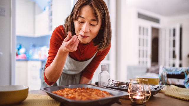 Woman tasting a dish of pasta she prepared while serving food on the table at home 