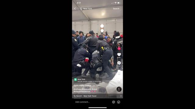 Several NYPD officers surround an individual on the ground inside a migrant shelter. 