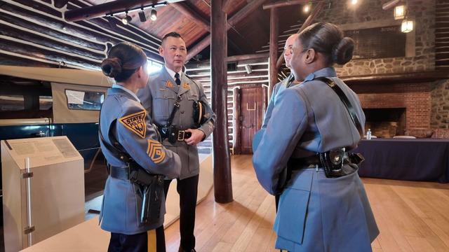Four New Jersey State Police troopers -- two men and two women -- stand in a room talking to each other. 