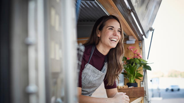 Smiling young woman looking away while standing in food truck at city 