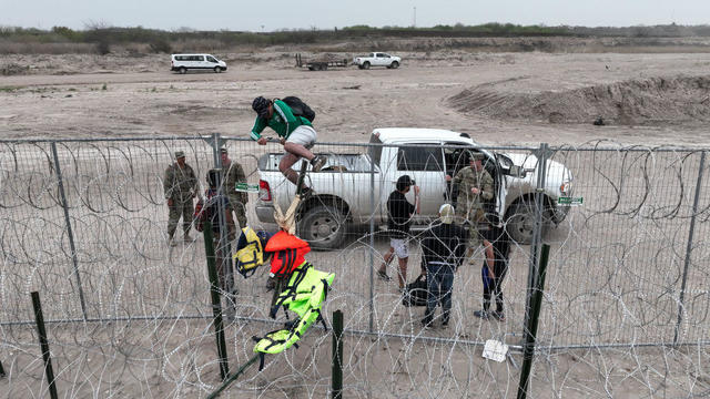 An aerial view shows a group of migrants climbing up wire fences in Eagle Pass, Texas, on Feb. 28, 2024. 