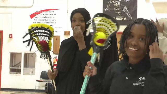 Two smiling female students hold lacrosse sticks 