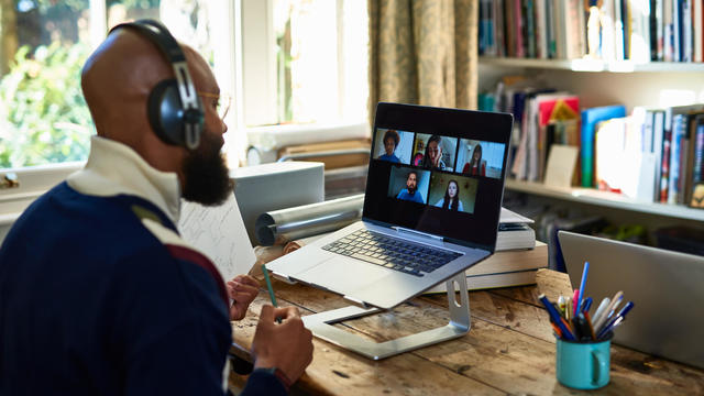 Black entrepreneur wearing headphones on video conference call on laptop in home office 