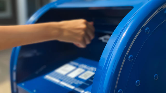 Woman mailing a letter in a blue U.S. Postal Service mailbox 
