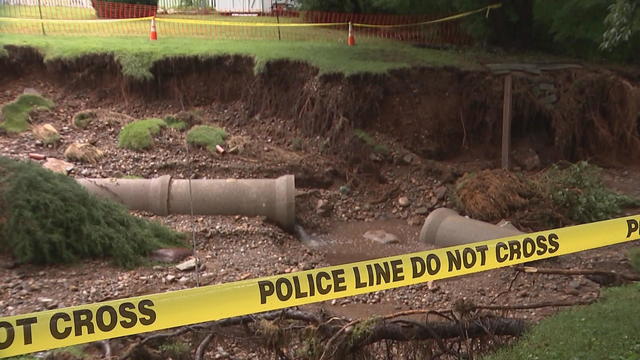 Police tape blocks off part of a backyard where flooding has exposed underground pipes 