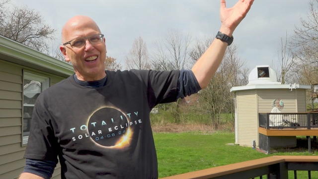 Peter Detterline in his backyard, smiling and gesturing with one hand toward the sky 