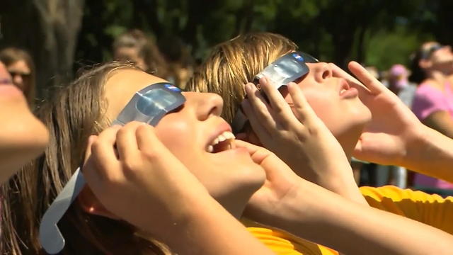 Two people outside looking up at the sky, wearing eclipse safety glasses 