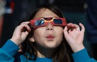 Miriam Toy looks through a pair of eclipse glasses that NASA was handing out as she awaits the eclipse on April 8, 2024, in Houlton, Maine. 