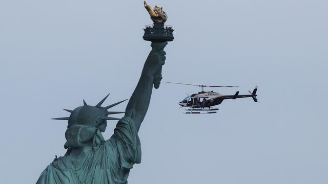 A doors off FlyNYON tourist helicopter flies past the Statue of Liberty at sunset in New York City on July 1, 2020 as seen from Jersey City, New Jersey. 