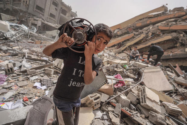 A Palestinian boy carries a gas cooker as he walks around the debris of a destroyed building in the city of Nuseirat in the central Gaza Strip on April 18, 2024, amid ongoing battles between Israel and the militant Hamas group. 