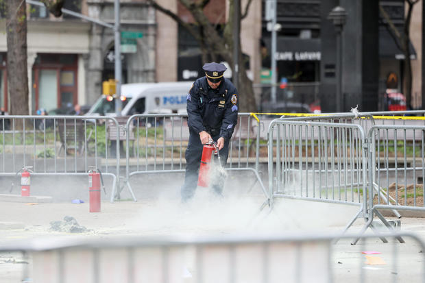 A police officer uses a fire extinguisher as emergency personnel respond to a fire outside the courthouse where former President Donald Trump's "hush money" trial is underway in New York, April 19, 2024. 