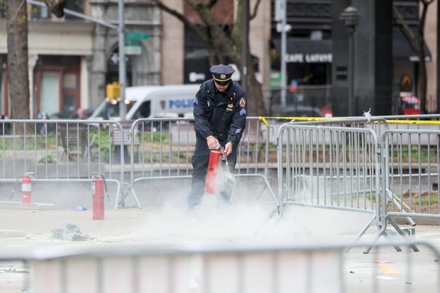 A police officer uses a fire extinguisher as emergency personnel respond to a fire outside the courthouse where former President Donald Trump's "hush money" trial is underway in New York, April 19, 2024. 