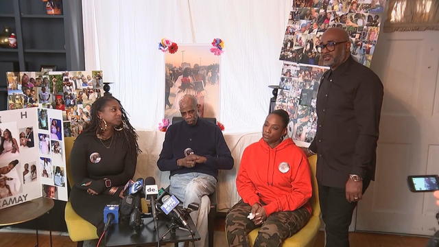 Three members of Camay Mitchell De Silva's family, surrounded by photos of Camay, speak to media from their home 