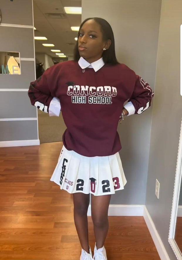 Camay Mitchell De Silva wearing a Concord High School sweatshirt and pleated skirt that says Class of 2023