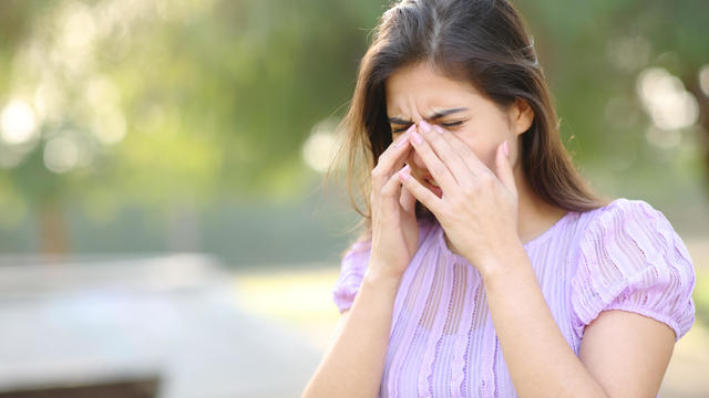 Allergic woman scratching eyes in a park 