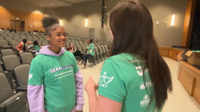 A student speaks to an adult, both are wearing green shirts that say Sean Strong 