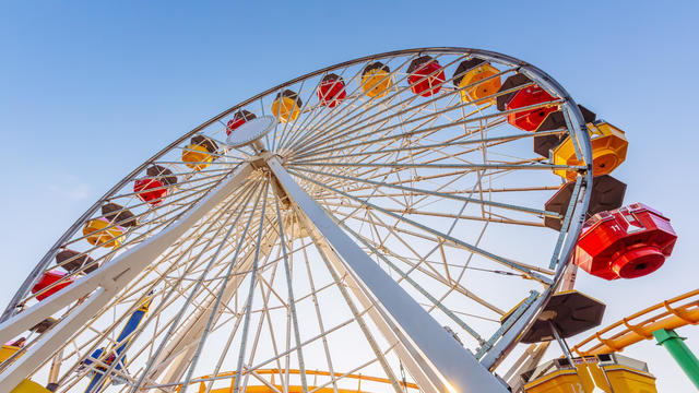 Low angle view of multi-coloured vibrant ferris wheel against blue sky 