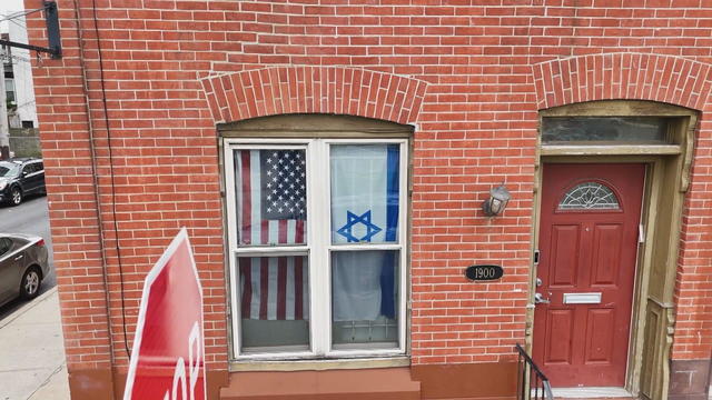 A brick house with an American flag and an Israeli flag in the windows. 
