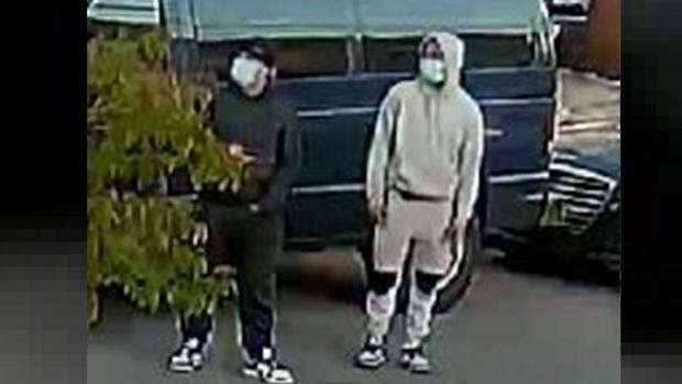 A surveillance photo shows two individuals wearing face masks standing in front of a van on a street. 