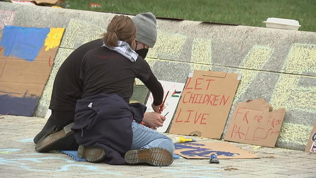 Two people sit on the ground making posters, one sign propped up in front of them says Let children live 