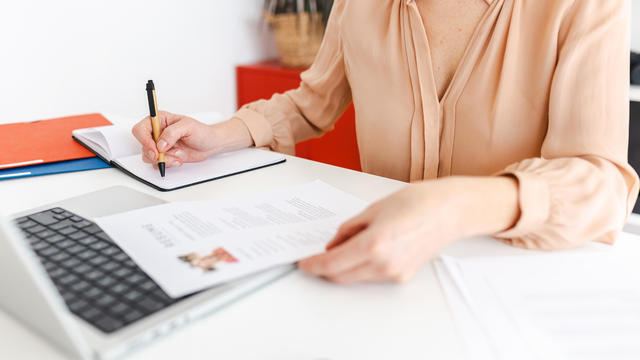 Close up view of female HR recruiter taking notes while reading job applicant resume in the office. 