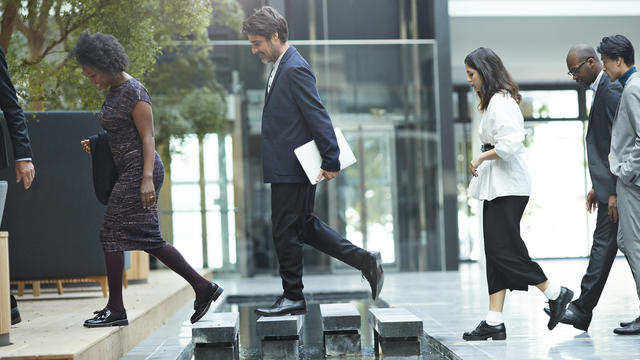 Business people crossing over step stones in atrium of modern office building 