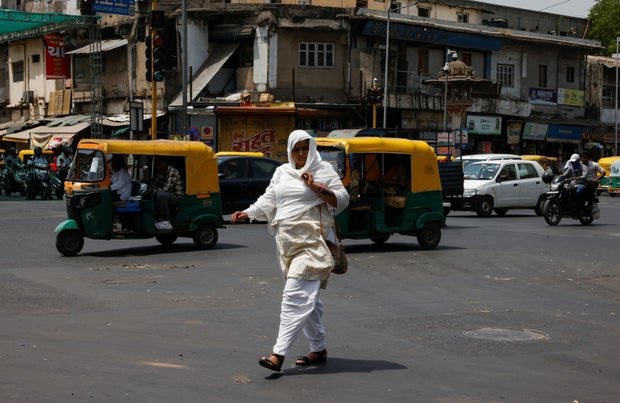 A woman covered with a cloth to protect herself from the heat walks on a road during a heat wave in Ahmedabad